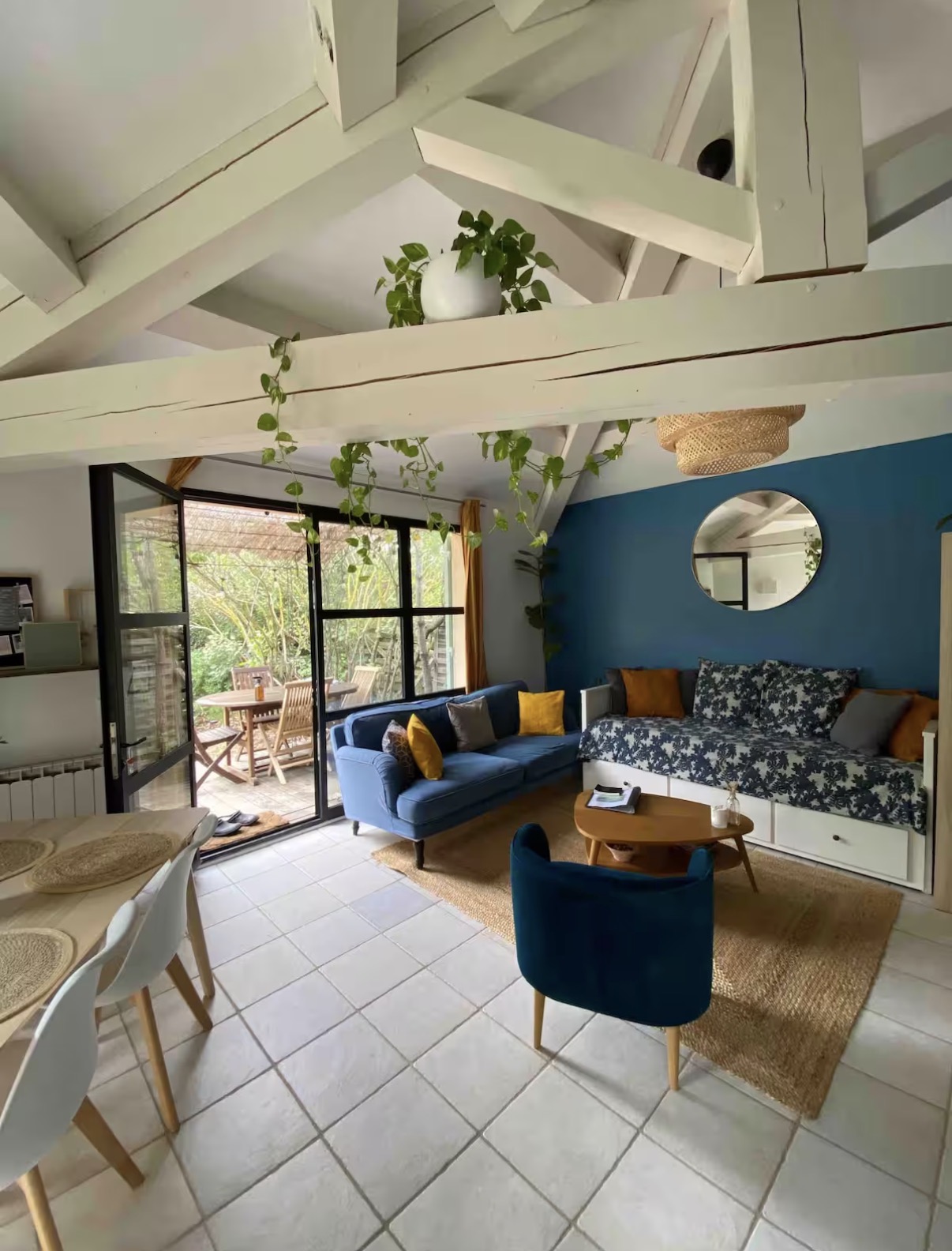 Salon lumineux de La Tanière, poutres blanches et mur bleu, ouvert sur la terrasse